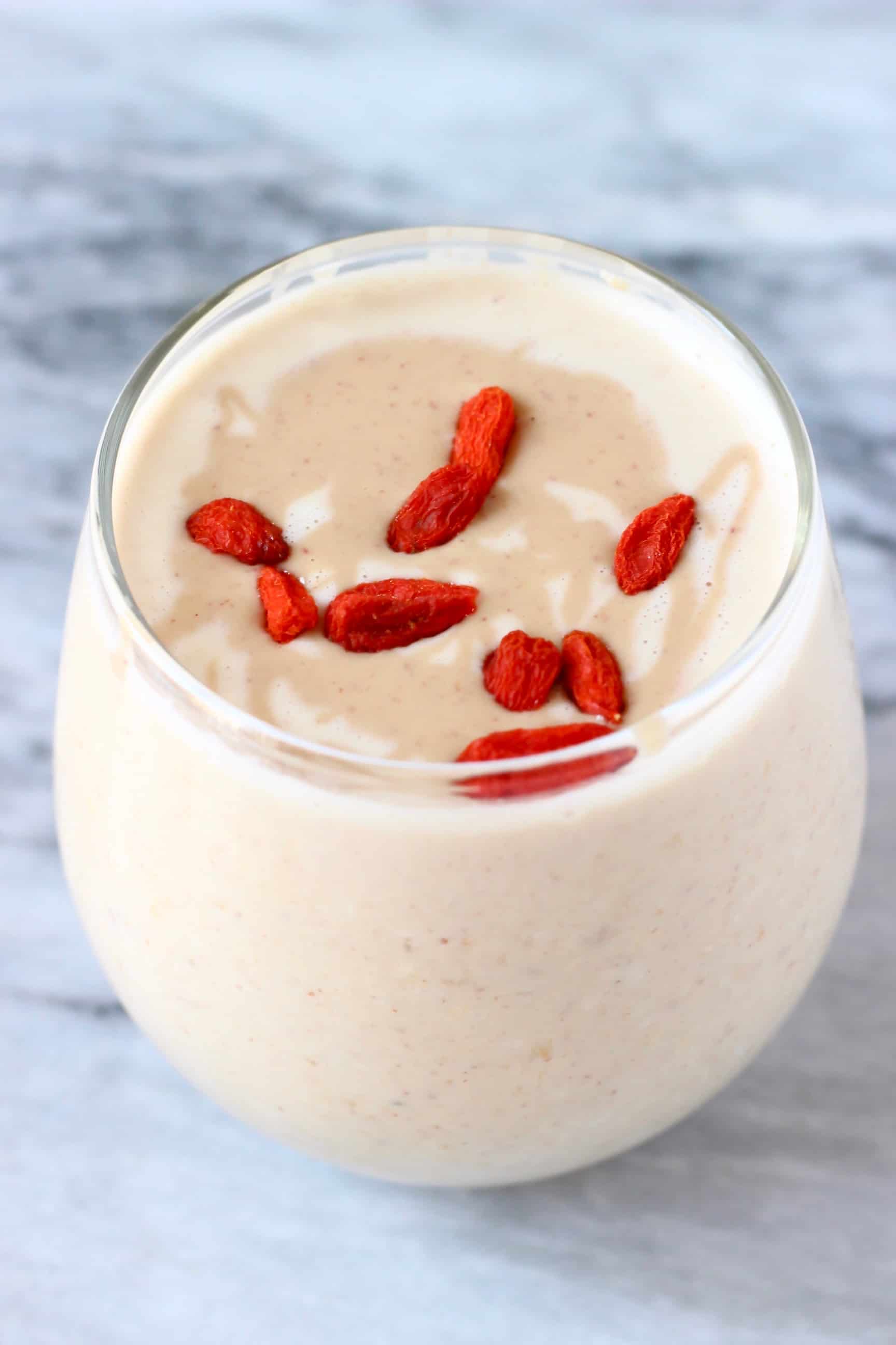 Peanut butter overnight oats topped with red goji berries in a small glass against a marble background