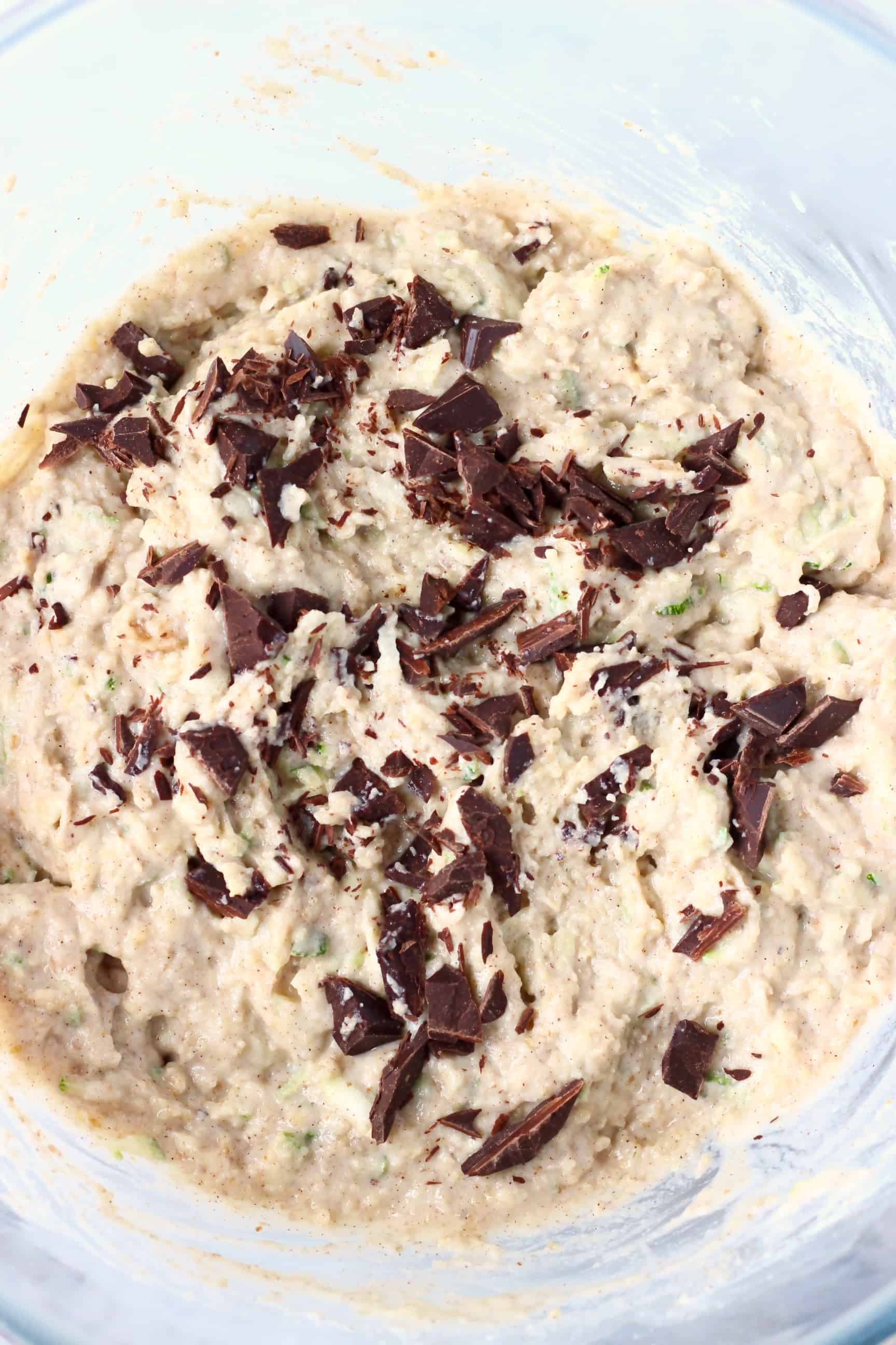 Raw zucchini muffin batter with chocolate chunks in a glass mixing bowl taken from above