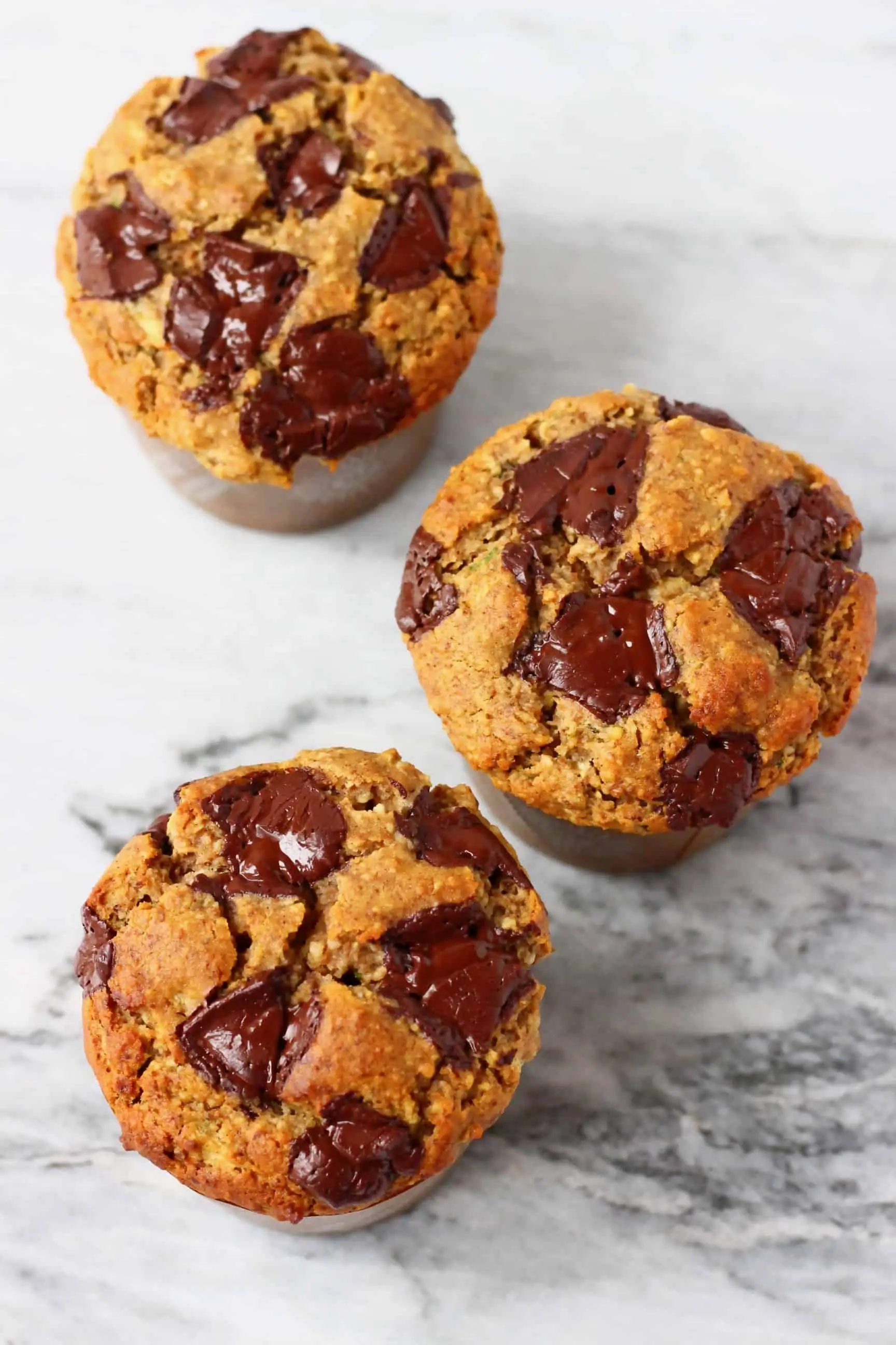 Three zucchini muffins with chocolate chips against a marble background