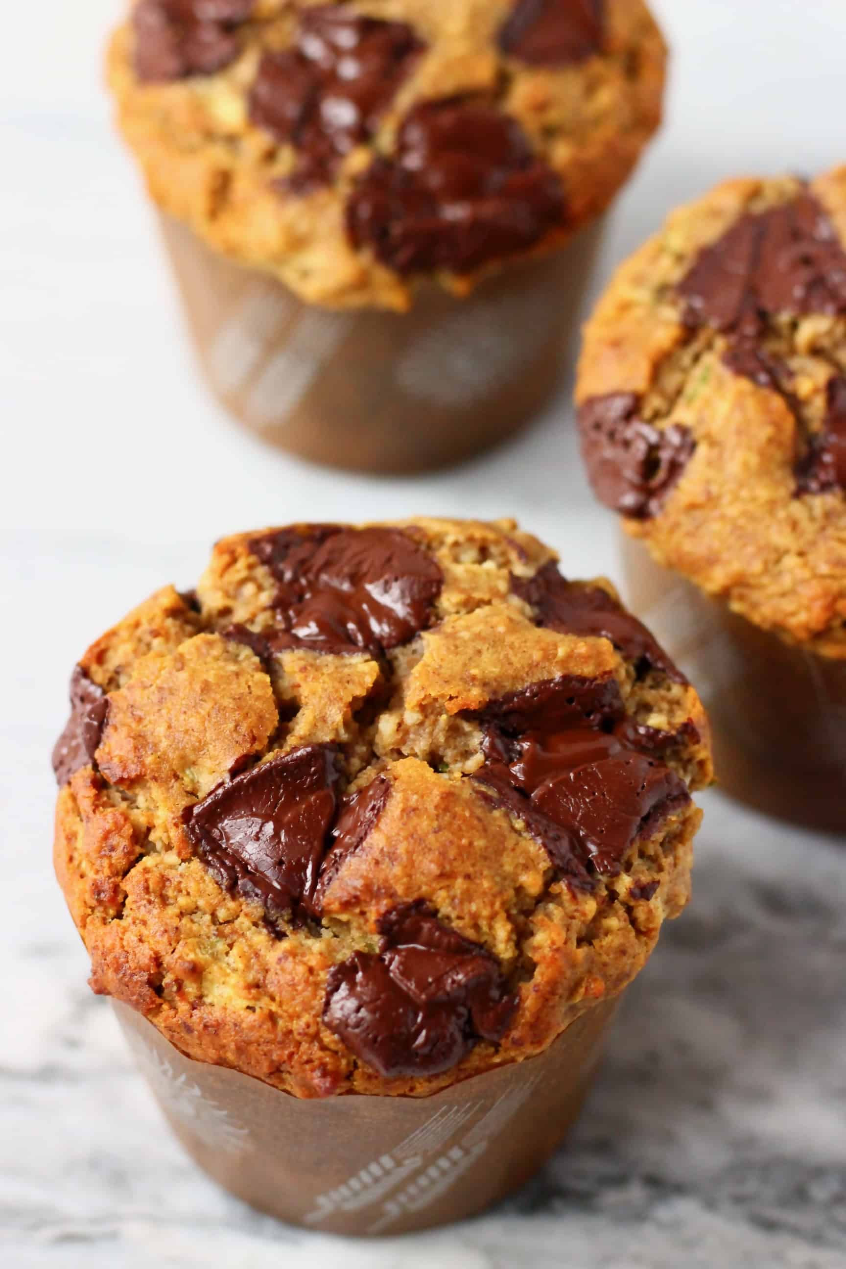 Three zucchini muffins with chocolate chips against a marble background