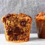 A gluten-free vegan zucchini muffin with chocolate chips cut in half on a marble slab against a grey background