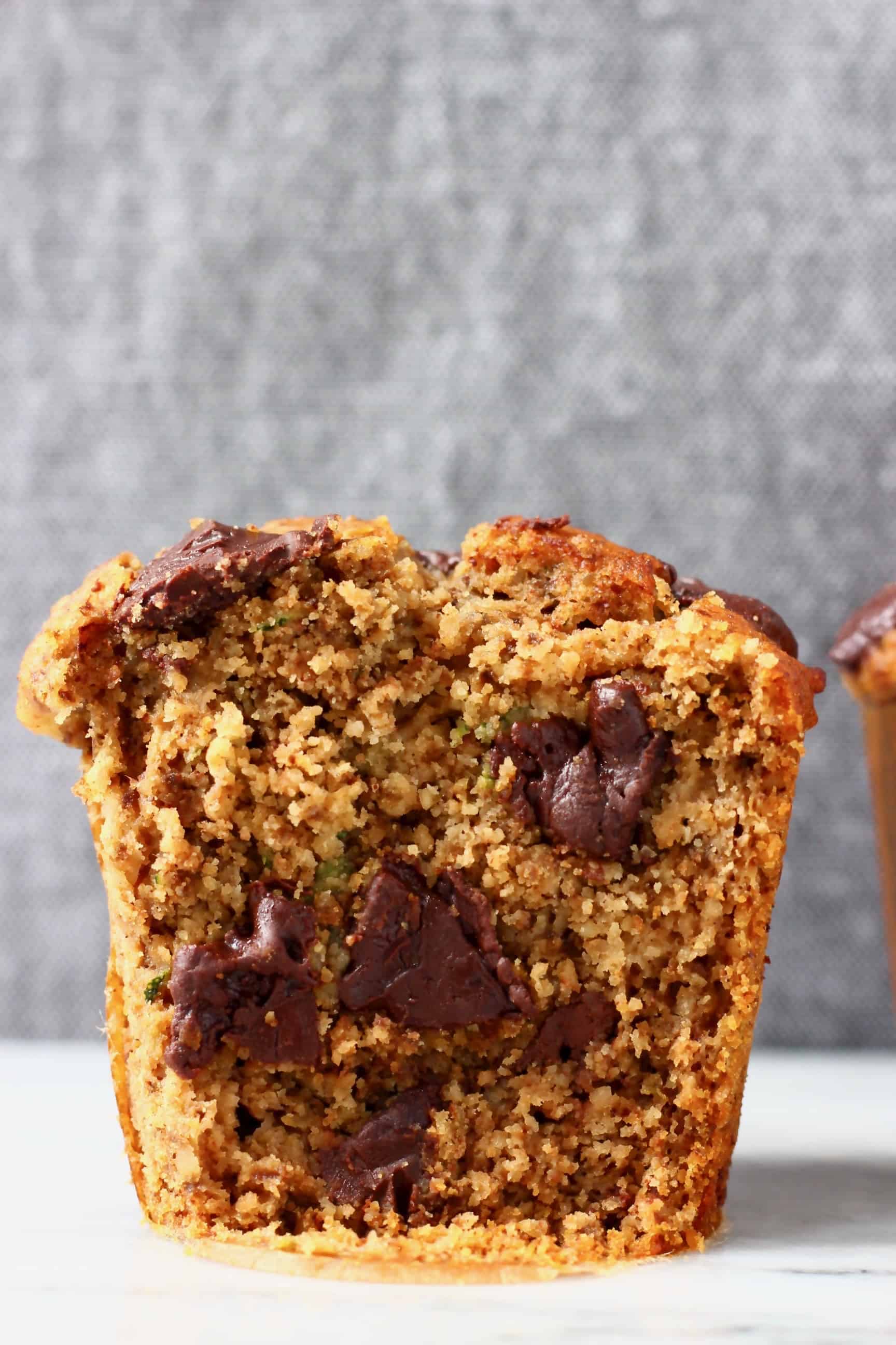 A gluten-free vegan zucchini muffin with chocolate chips cut in half on a marble slab against a grey background