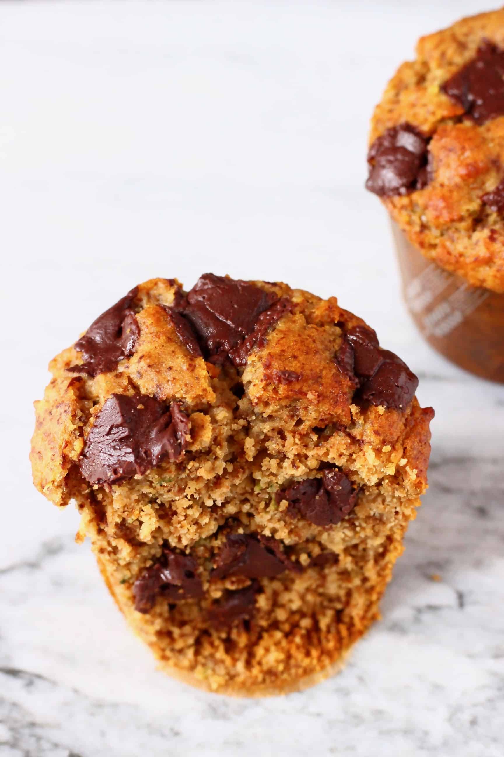 Two zucchini muffins with chocolate chips against a marble background