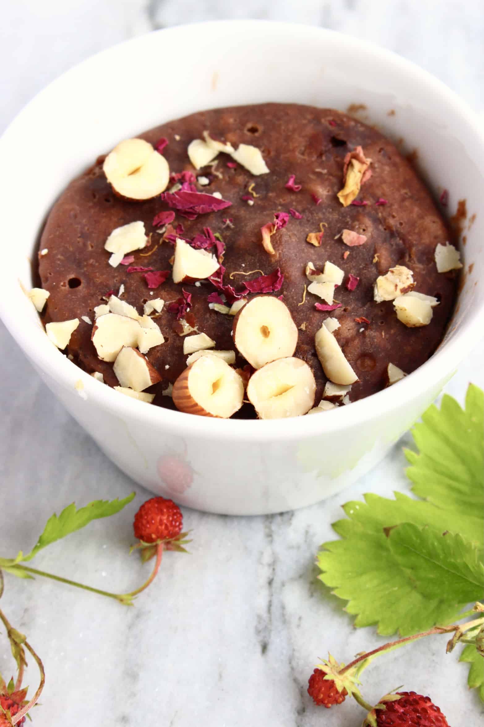 A vegan chocolate mug cake in a white mug topped with chopped hazelnuts