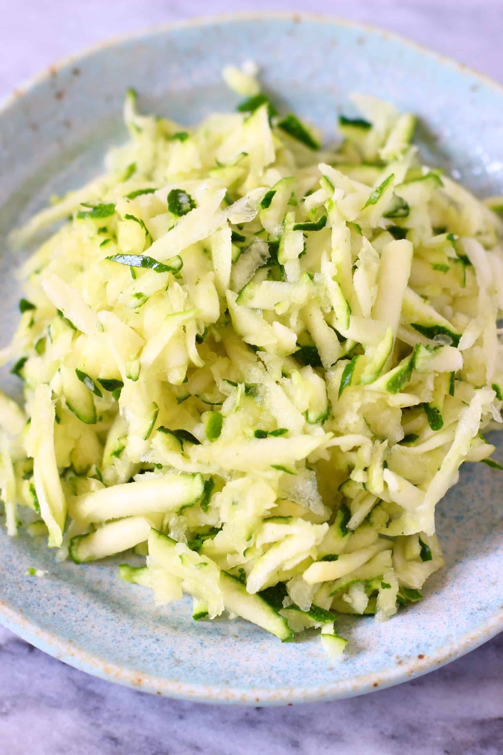 A pile of grated zucchini on a blue plate against a marble background