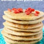 A stack of banana oatmeal pancakes decorated with goji berries on a green plate against a grey background