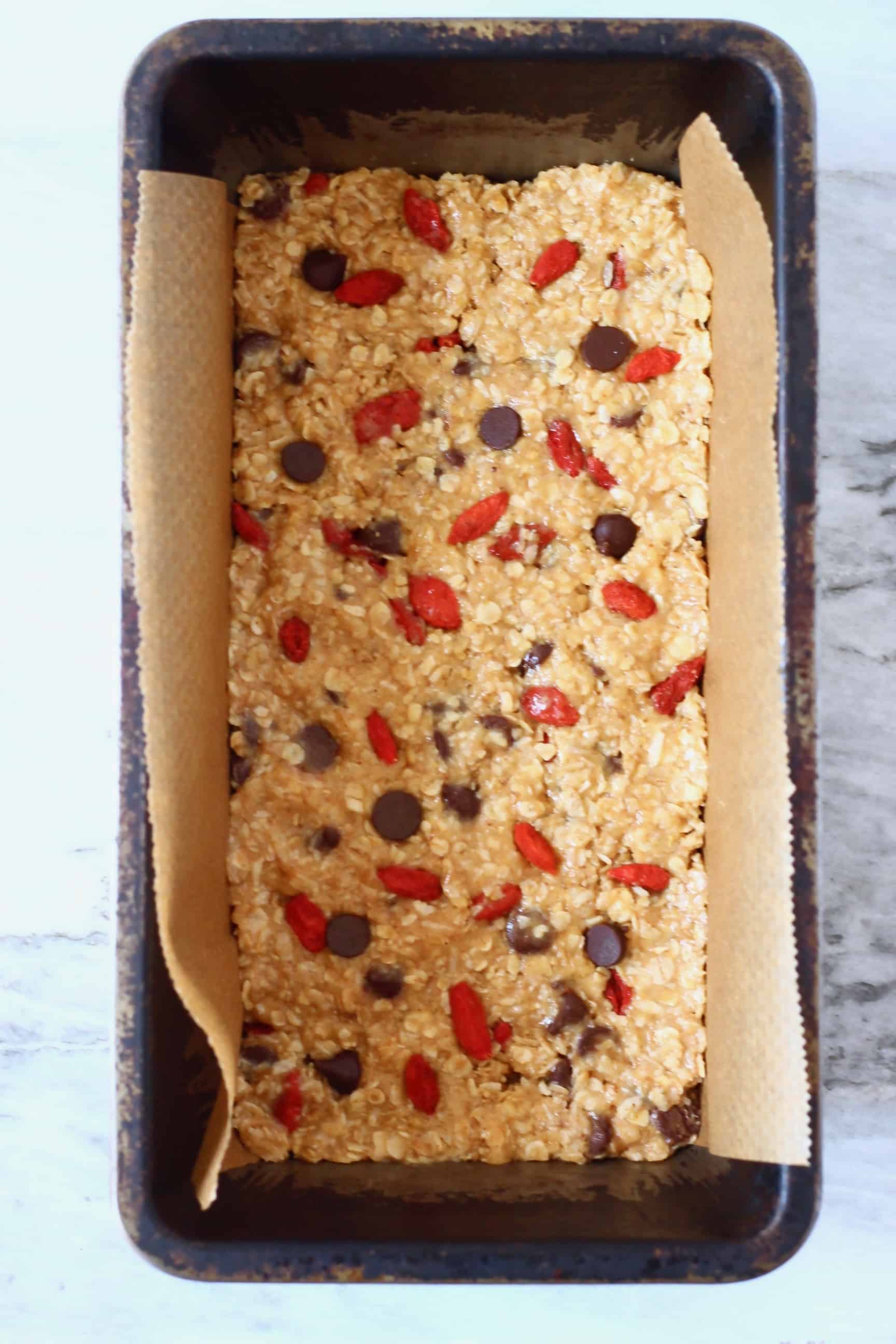 No-bake granola bar mixture with chocolate chips and goji berries in a loaf tin lined with baking paper