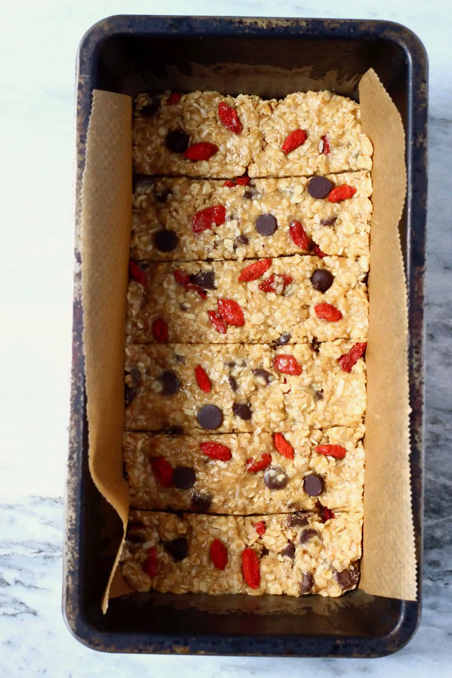 No-bake granola bar mixture with chocolate chips and goji berries cut into six bars in a loaf tin lined with  baking paper