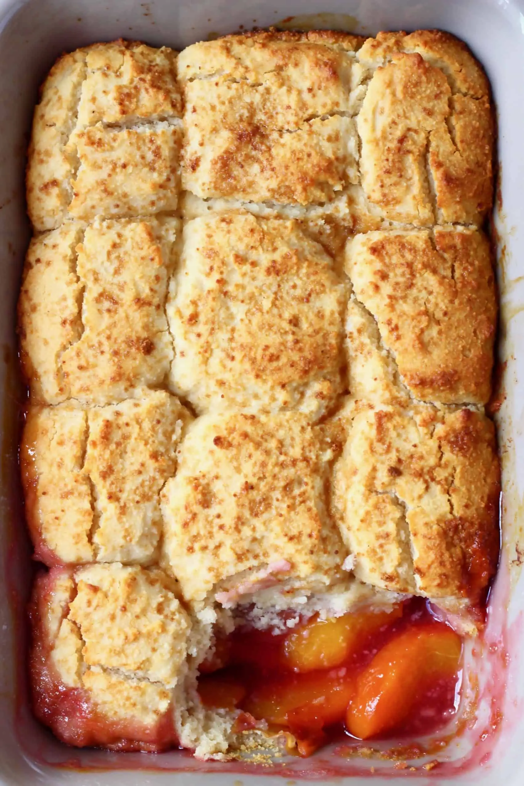 Peach cobbler in a rectangular grey baking tray with a spoonful taken out of it