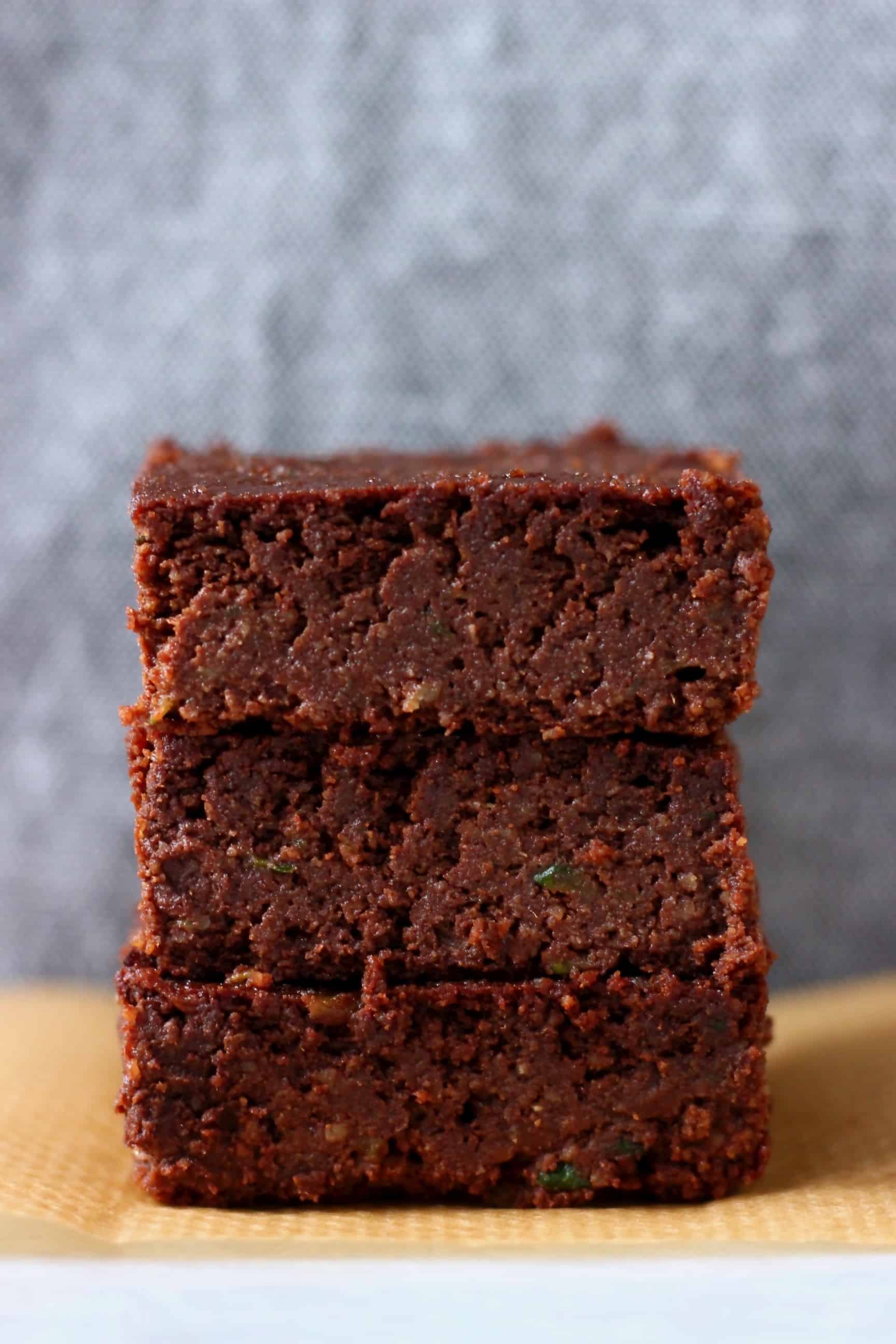 Three vegan zucchini brownies stacked up on top of each other on a sheet of baking paper 