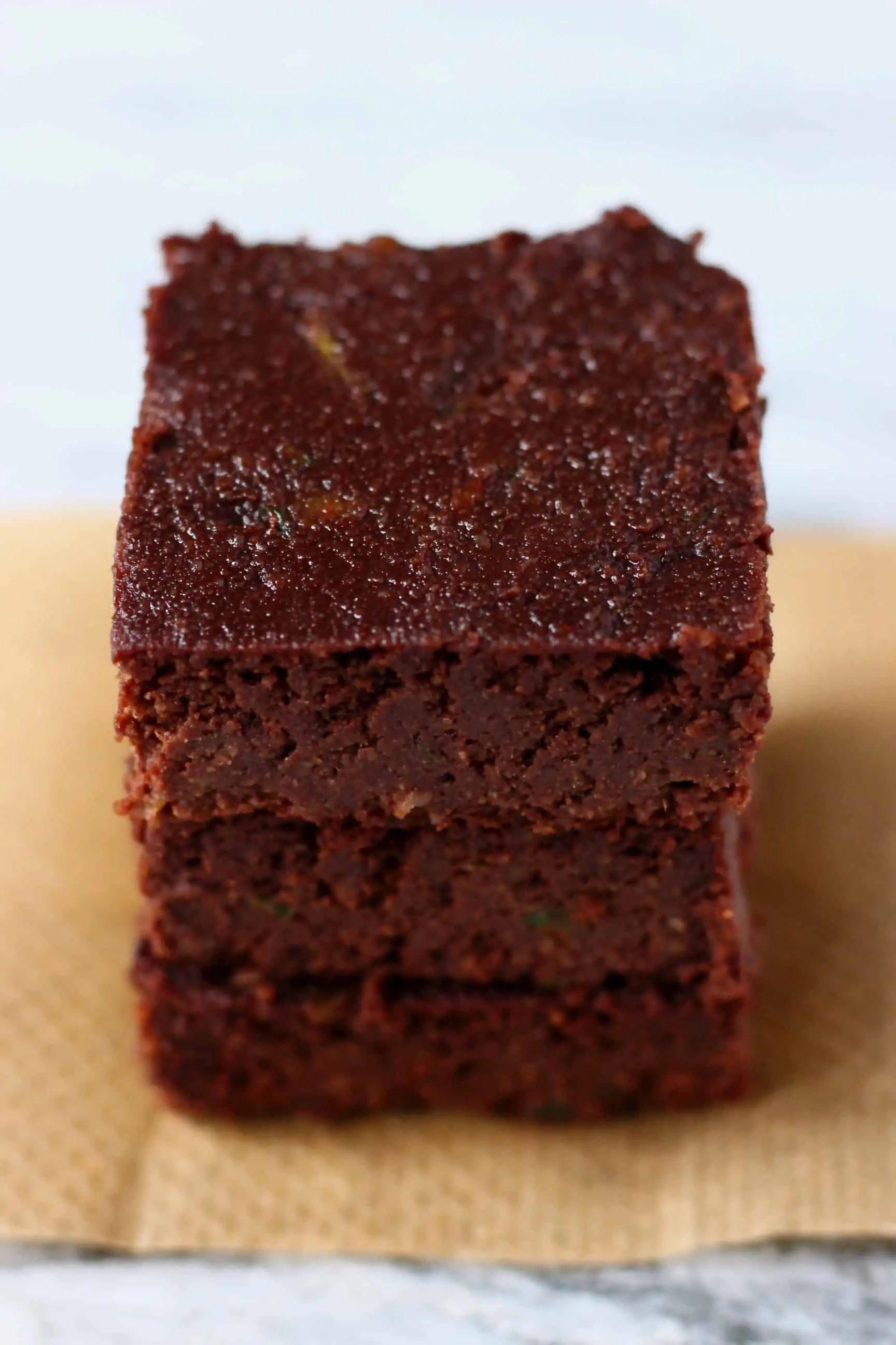 Three vegan zucchini brownies stacked up on top of each other on a sheet of brown baking paper 