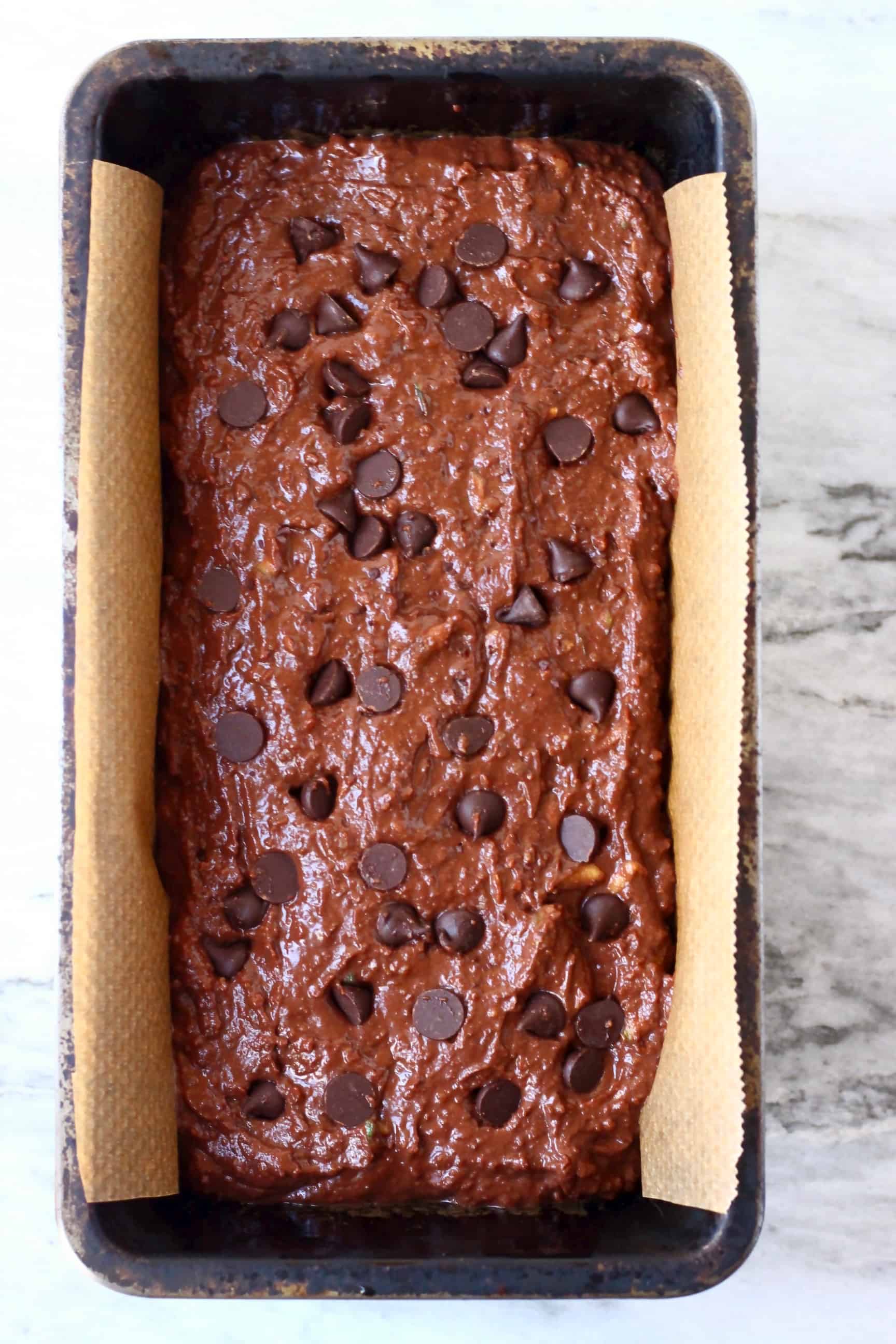Raw gluten-free vegan chocolate zucchini bread batter studded with chocolate chips in a loaf tin lined with baking paper