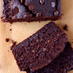 A loaf of gluten-free vegan chocolate zucchini bread studded with chocolate chips with two slices next to it