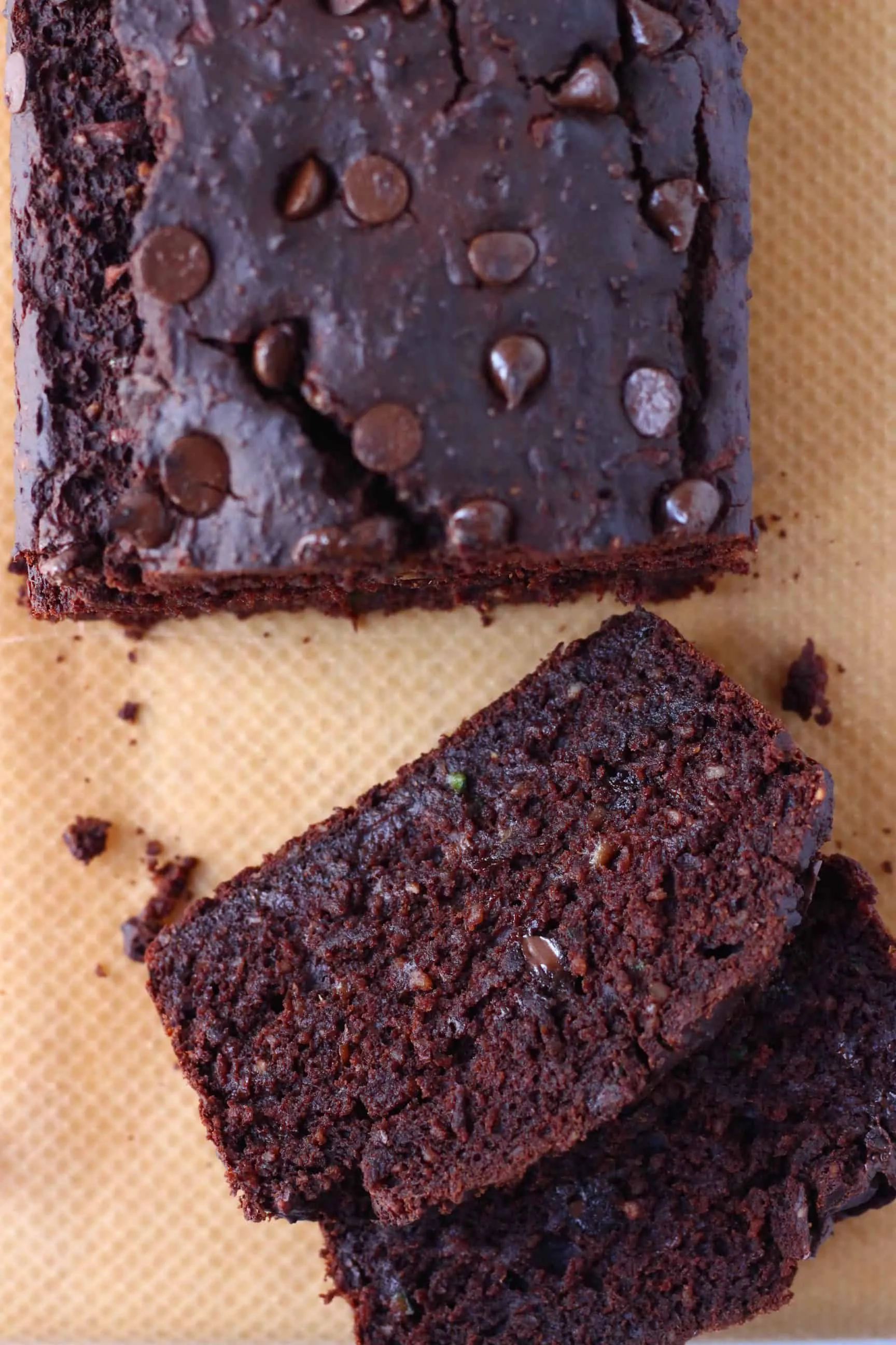 A loaf of gluten-free vegan chocolate zucchini bread studded with chocolate chips with two slices next to it