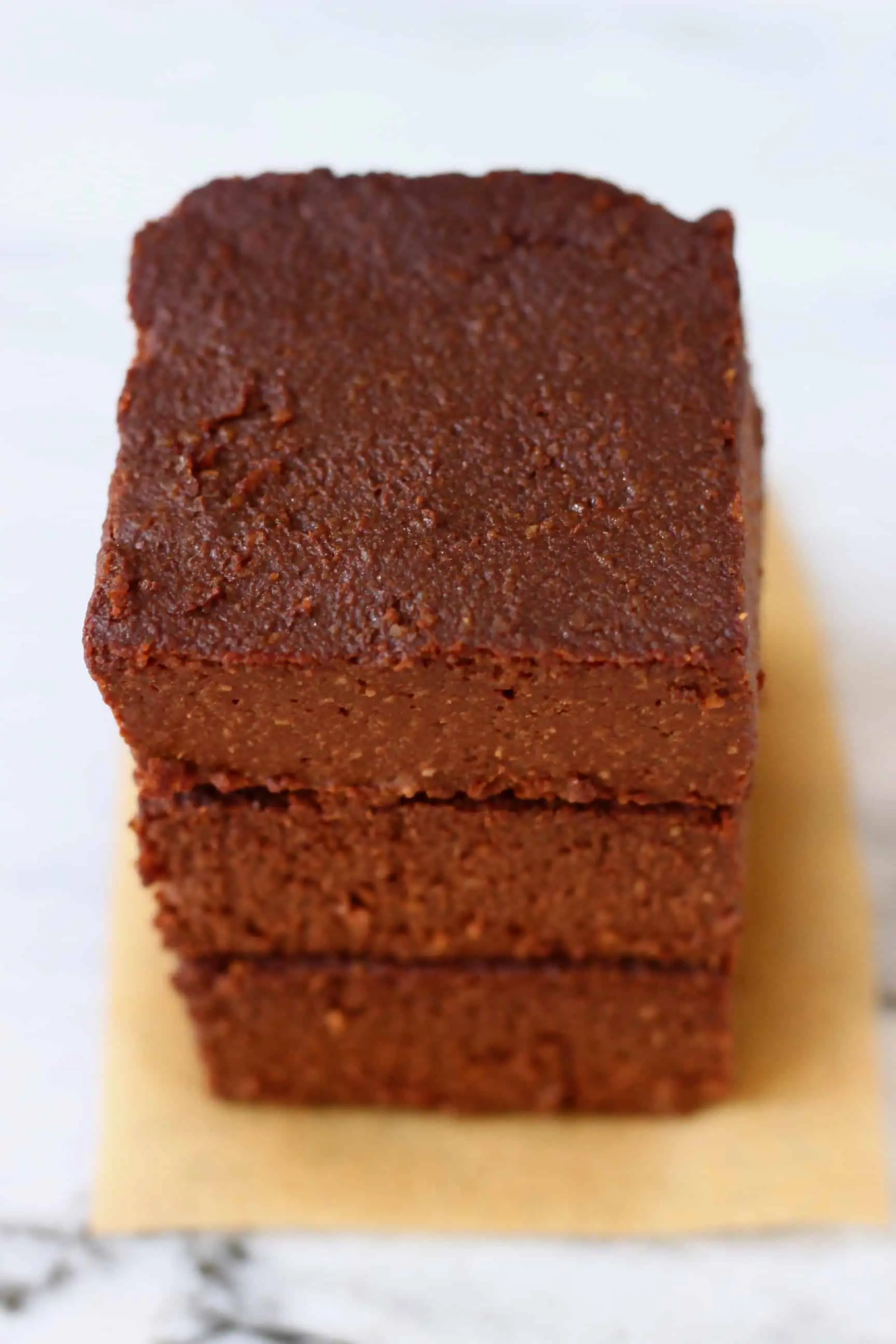Three pumpkin brownies stacked on top of each other on a sheet of brown baking paper against a marble background
