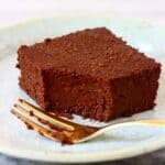 A pumpkin brownie with a mouthful taken out of it on a light blue plate with a gold fork