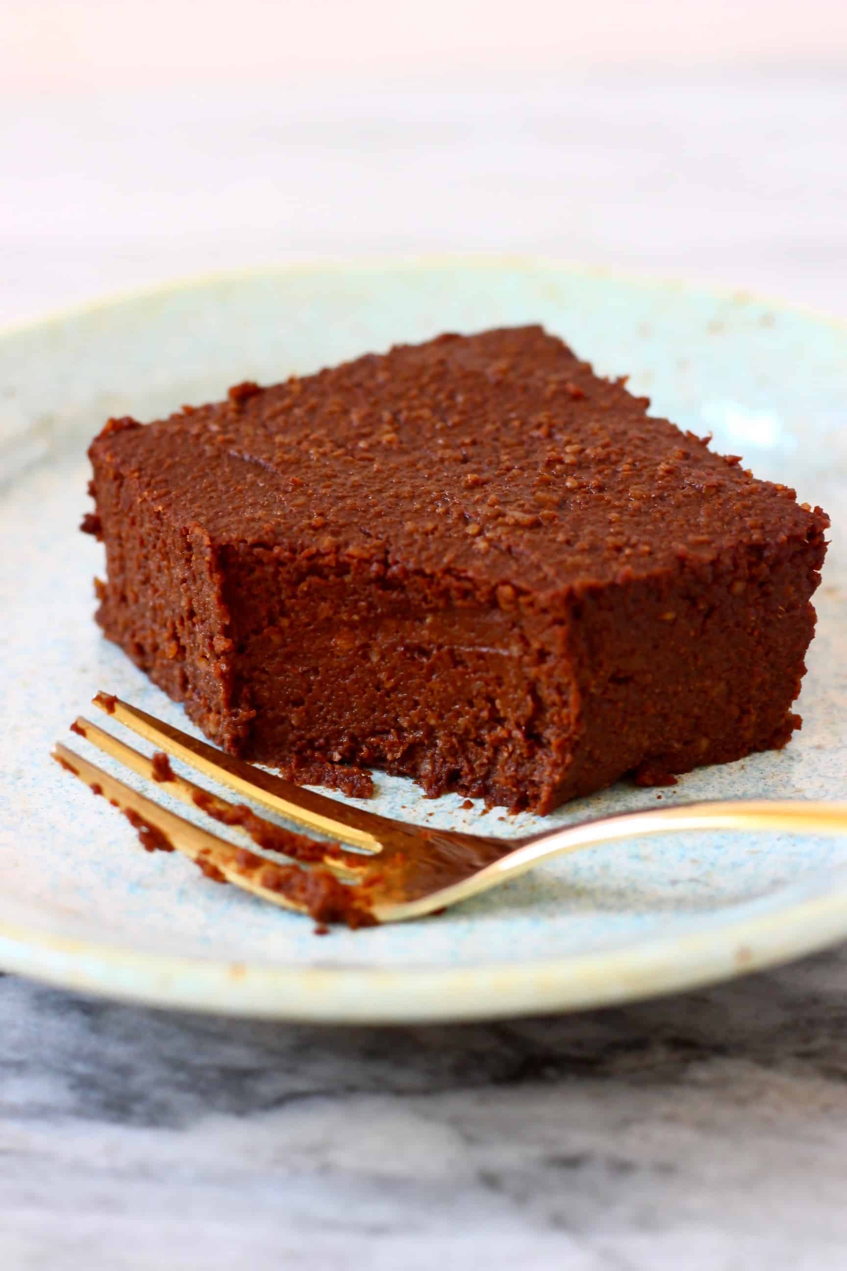 A pumpkin brownie with a mouthful taken out of it on a light blue plate with a gold fork