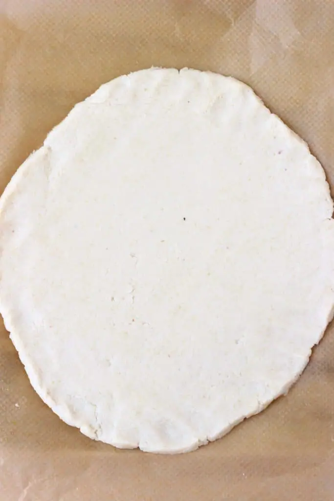 A circle of pastry dough rolled out on a sheet of brown baking paper