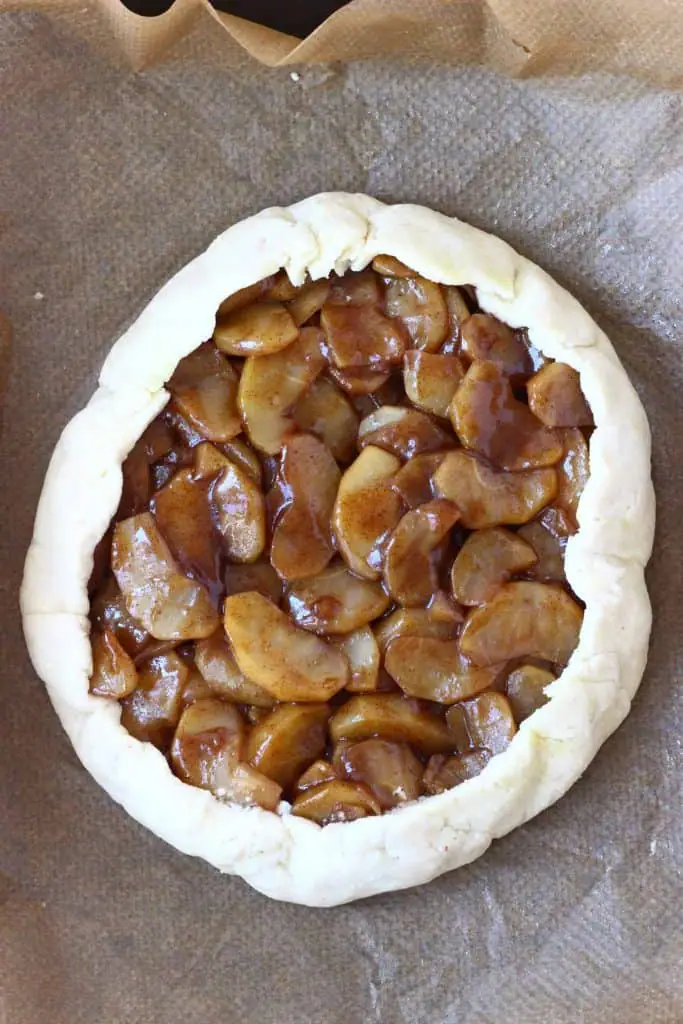 A raw apple galette against a sheet of brown baking paper