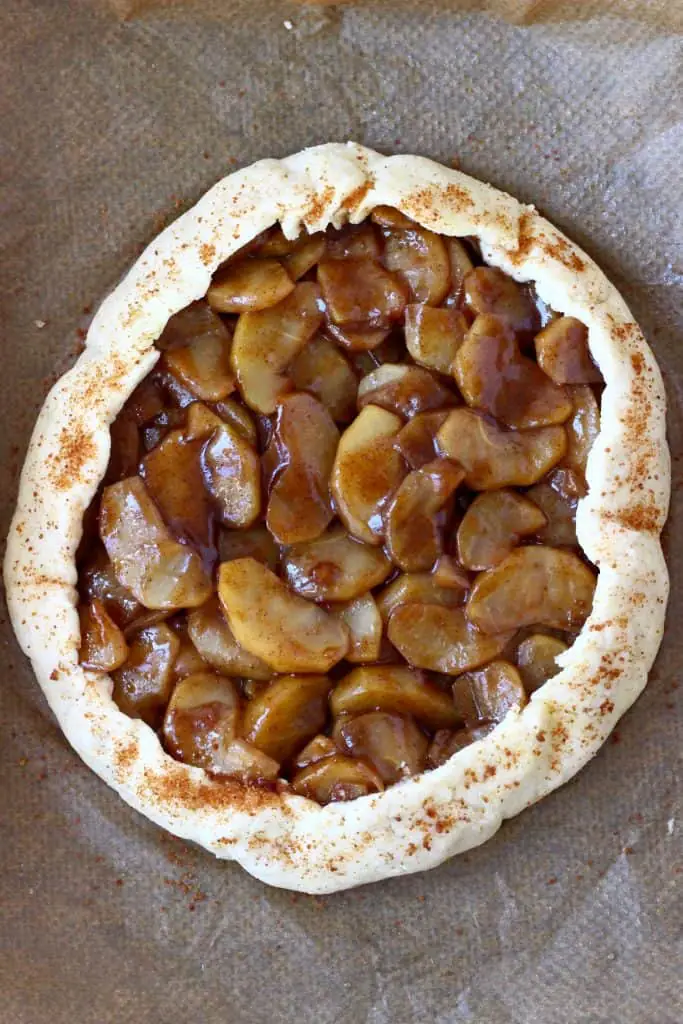 A raw apple galette sprinkled with coconut sugar against a sheet of brown baking paper