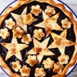 Cherry pie topped with stars and flowers in a white pie dish with a blue rim against a marble background