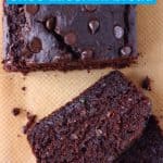 A loaf of chocolate zucchini bread studded with chocolate chips with two slices taken from it against a sheet of brown baking paper