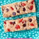Two light brown granola bars studded with chocolate chips and goji berries on a green plate