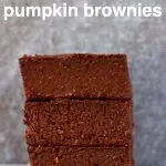 Three pumpkin brownies stacked on top of each other on a sheet of brown baking paper against a grey background