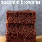 Three zucchini brownies stacked up on top of each other on a sheet of brown baking paper against a grey background