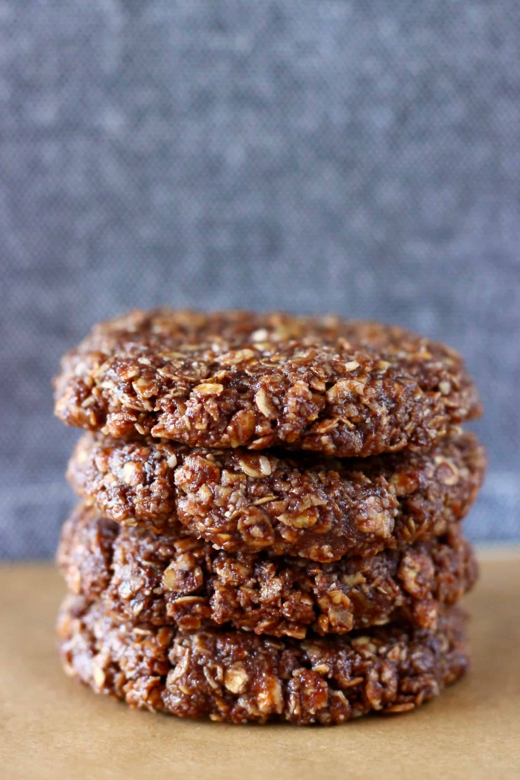 Four raw chocolate oatmeal cookies stacked on top of each other on a sheet of brown baking paper against a grey background