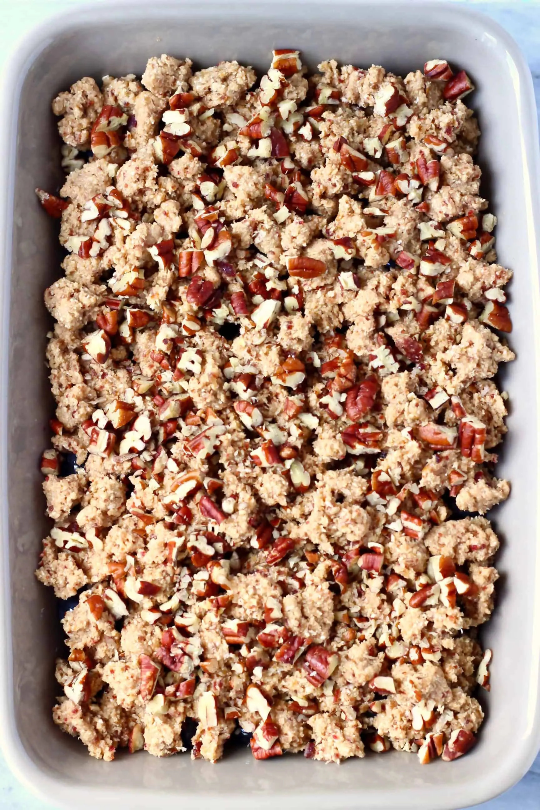 Raw blueberry crisp topped with pecan nuts in a grey baking dish
