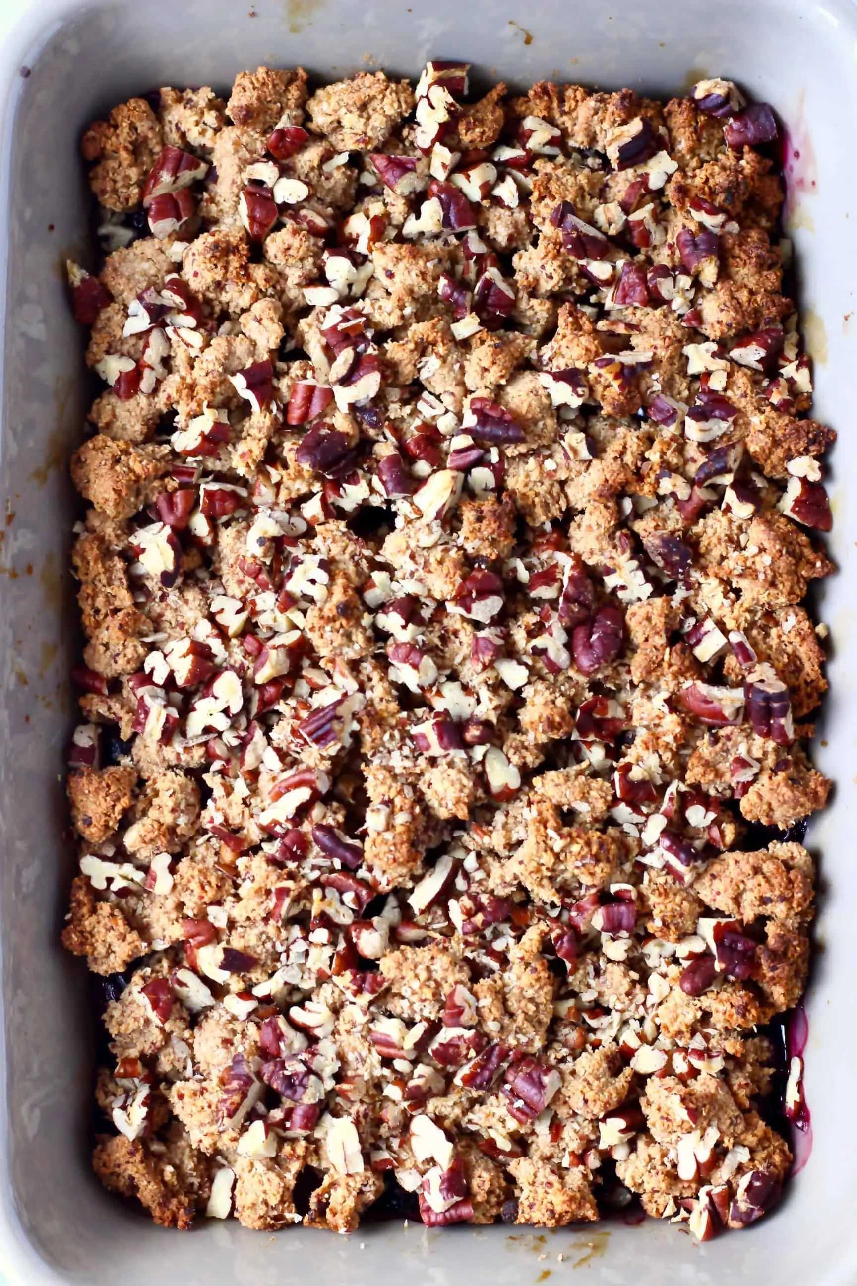 A grey rectangular baking dish with blueberry crisp topped with pecan nuts