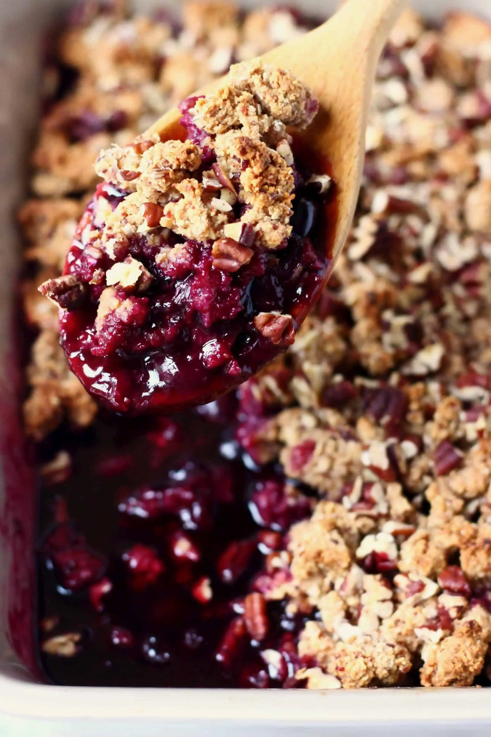 A grey rectangular baking dish of blueberry crisp with a wooden spoon lifting up a mouthful of it