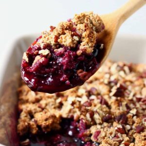 A grey rectangular baking dish of blueberry crisp with a wooden spoon lifting up a mouthful of it