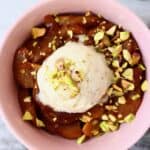 Sliced baked apples in a bowl scattered with chopped pistachio nuts and topped with ice cream