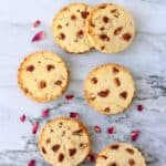 Six round coconut flour cookies with pecan nuts against a marble background scattered with rose petals