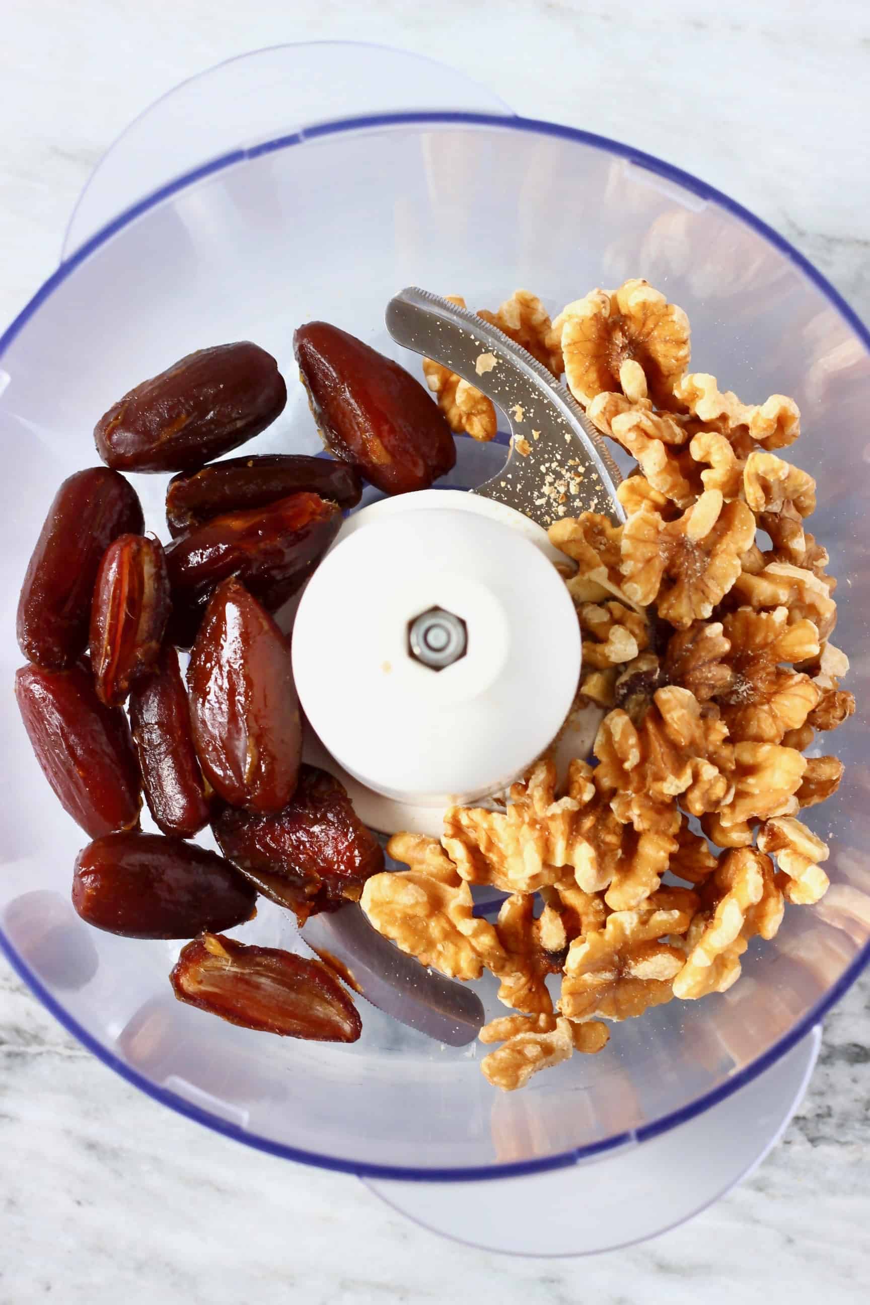 Dates, walnuts and salt in a food processor against a marble background