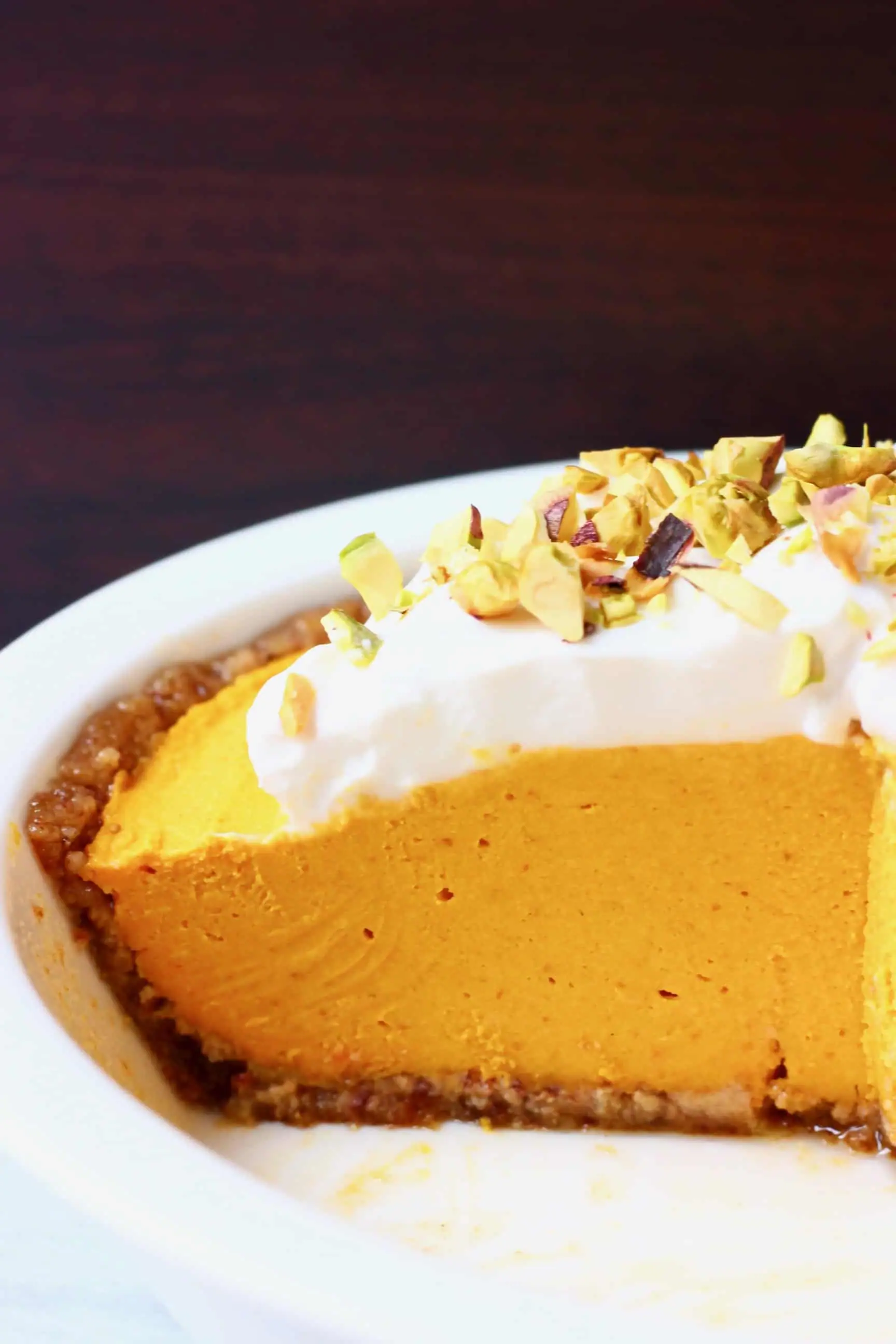 A white pie dish with no-bake vegan pumpkin pie topped with whipped cream and chopped pistachios 