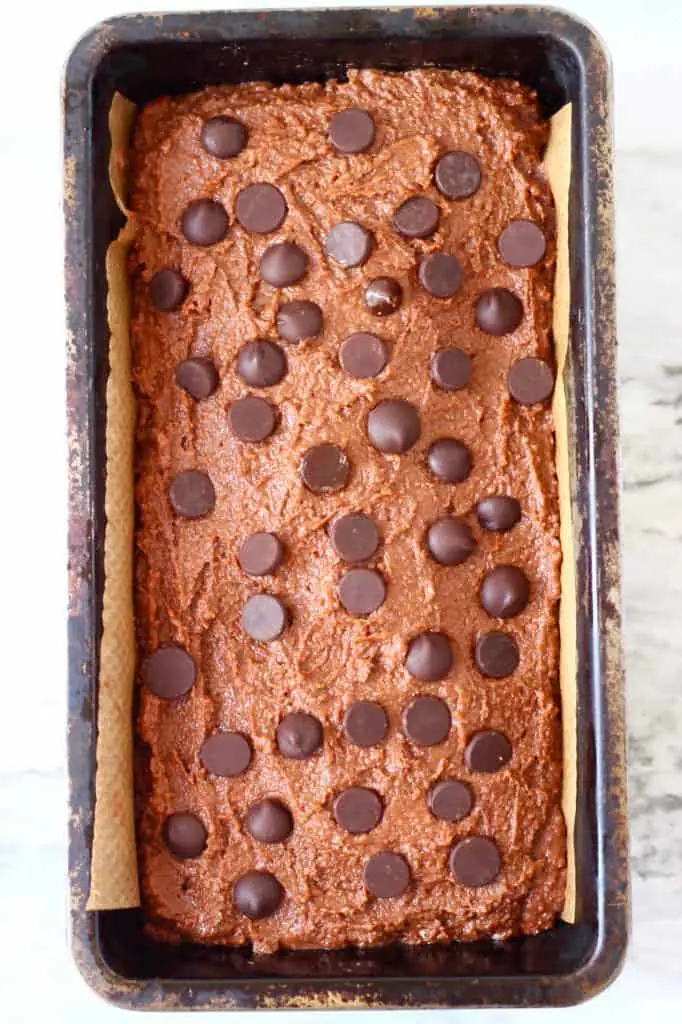Raw chocolate pumpkin bread with chocolate chips in a black loaf tin against a marble background