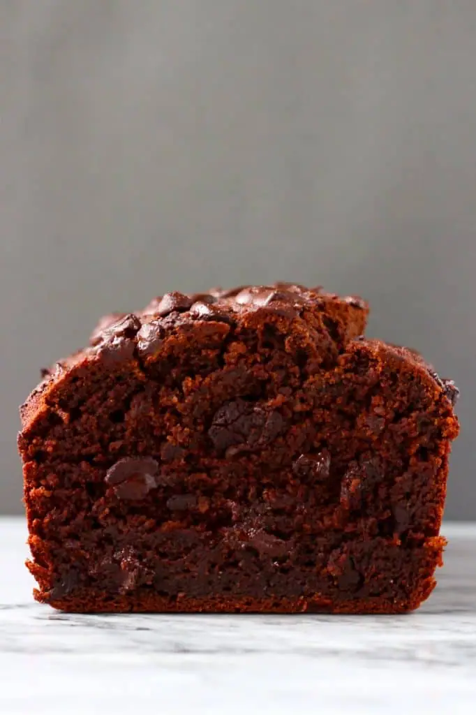 A loaf of chocolate pumpkin bread with chocolate chips on a marble slab against a grey background
