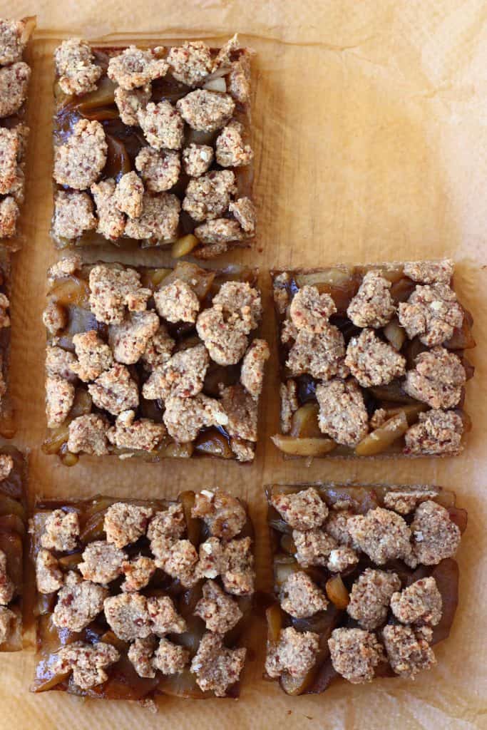Five square apple crumble bars against a sheet of brown baking paper