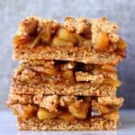 A stack of three apple crumble bars on a marble slab against a grey background