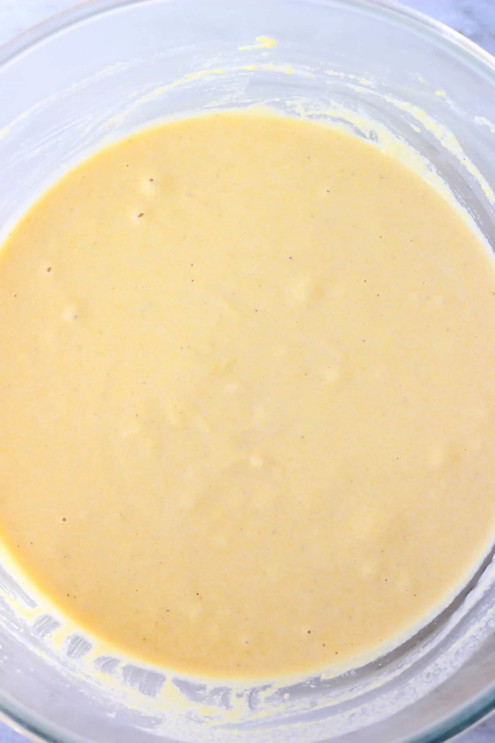 Raw gluten-free vegan cornbread muffin batter in a glass mixing bowl against a marble background