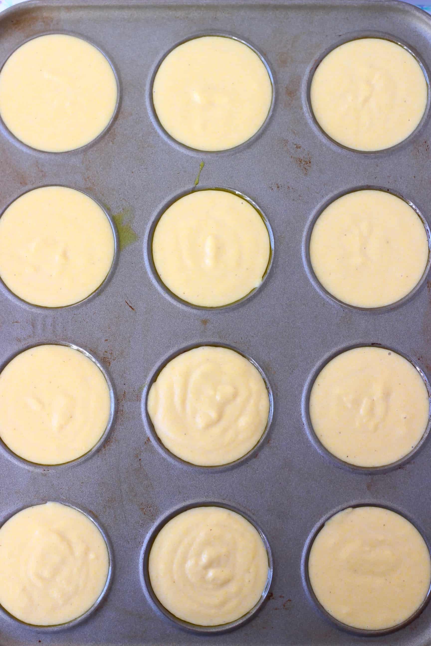 Raw gluten-free vegan cornbread muffin batter in twelve holes in a grey muffin tin