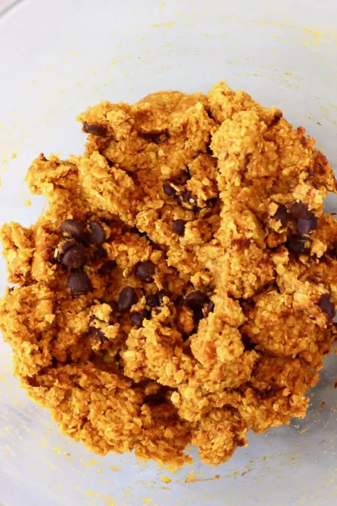 Raw pumpkin cookie dough in a glass mixing bowl against a marble background