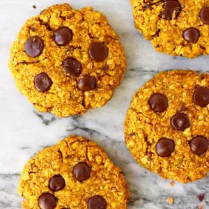Five pumpkin cookies with chocolate chips against a marble background