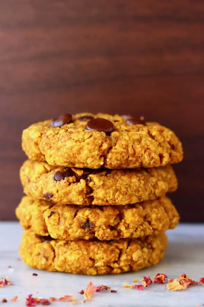 A stack of four orange pumpkin cookies studded with chocolate chips on a marble slab against a dark brown background