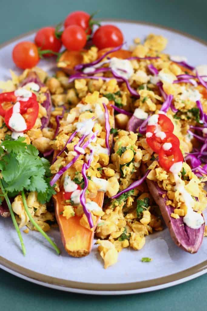Baked sweet potatoes scattered with smashed chickpeas and a white tahini dressing on a grey plate against a dark green background