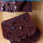 A loaf of chocolate pumpkin bread with two slices next to it against a sheet of brown baking paper