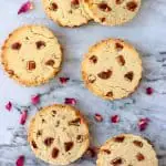 Six round cookies with pecan nuts against a marble background scattered with rose petals
